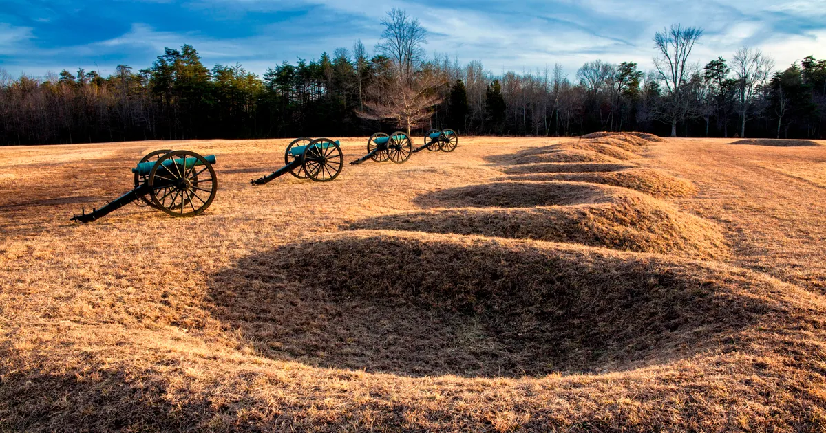 A line of four cannons placed in front of crescent shaped earthen gun pits.