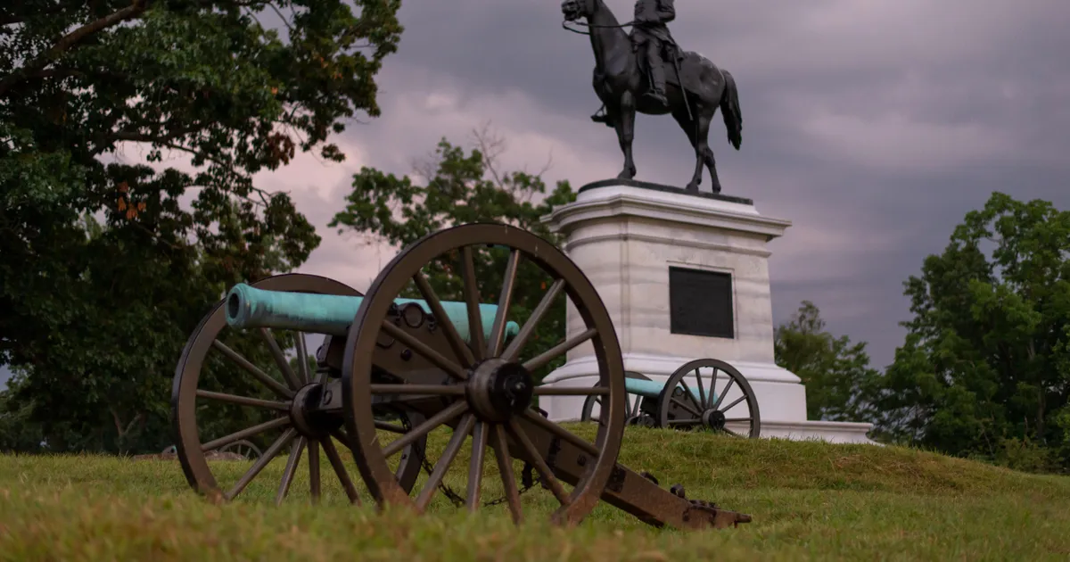 A canon sits in front of an equestrian statue.