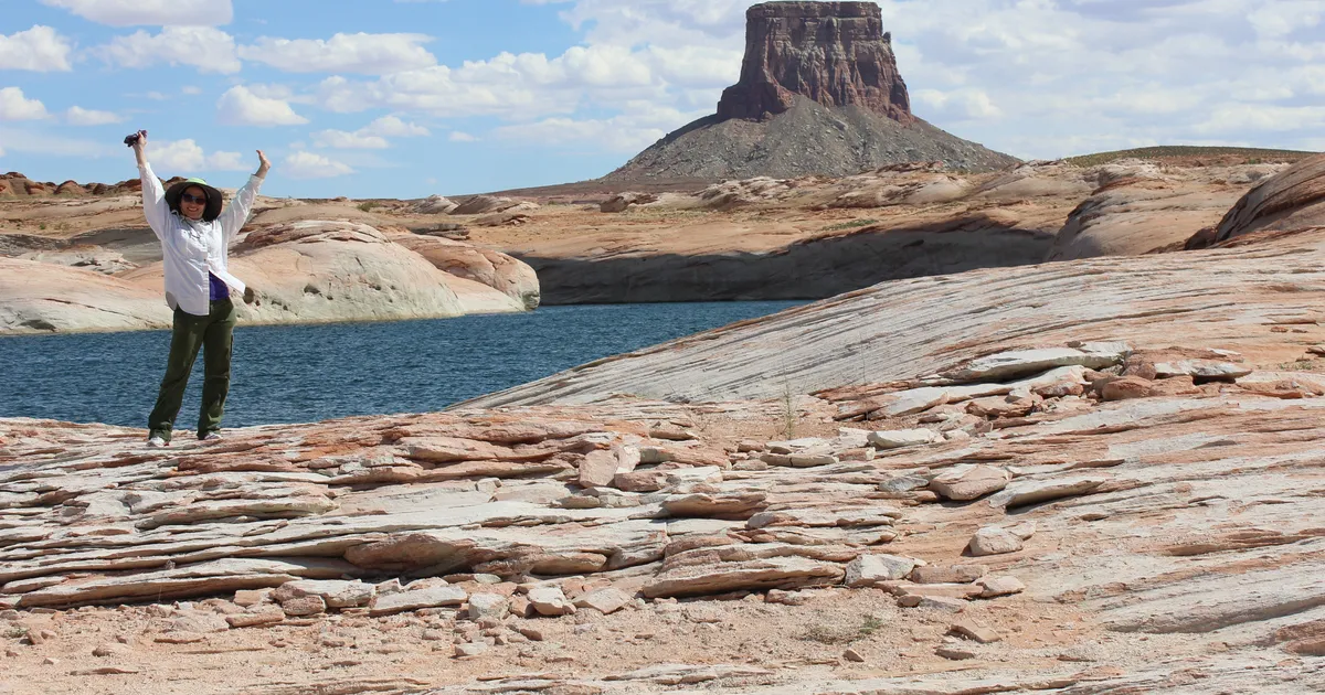 Woman raises her arms while standing in front of a sandstone butte