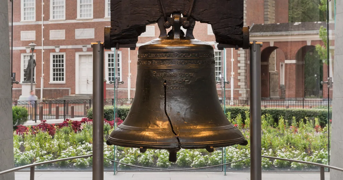 Color photo of the Liberty Bell with Independence Hall in the background.