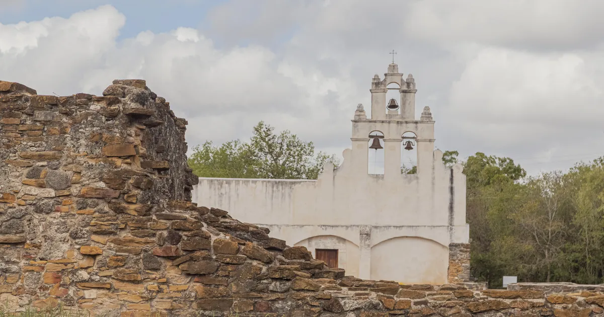 White frescoed church with a stone ruin to the left in the foreground.