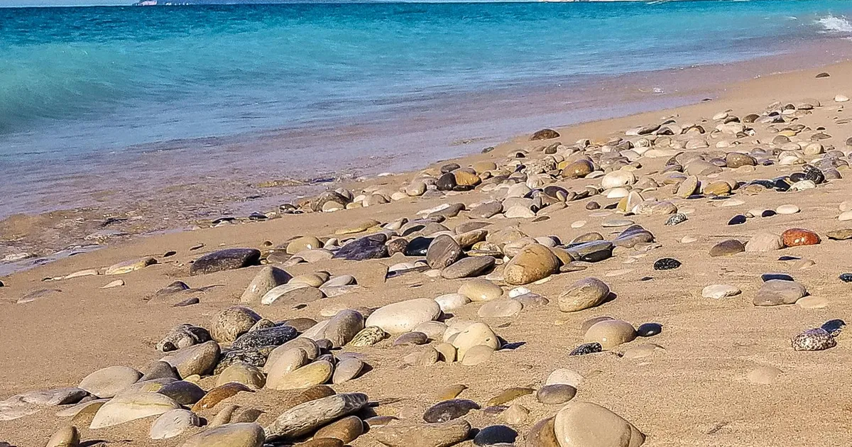 Sand and pebbles in foreground with turquoise water in background